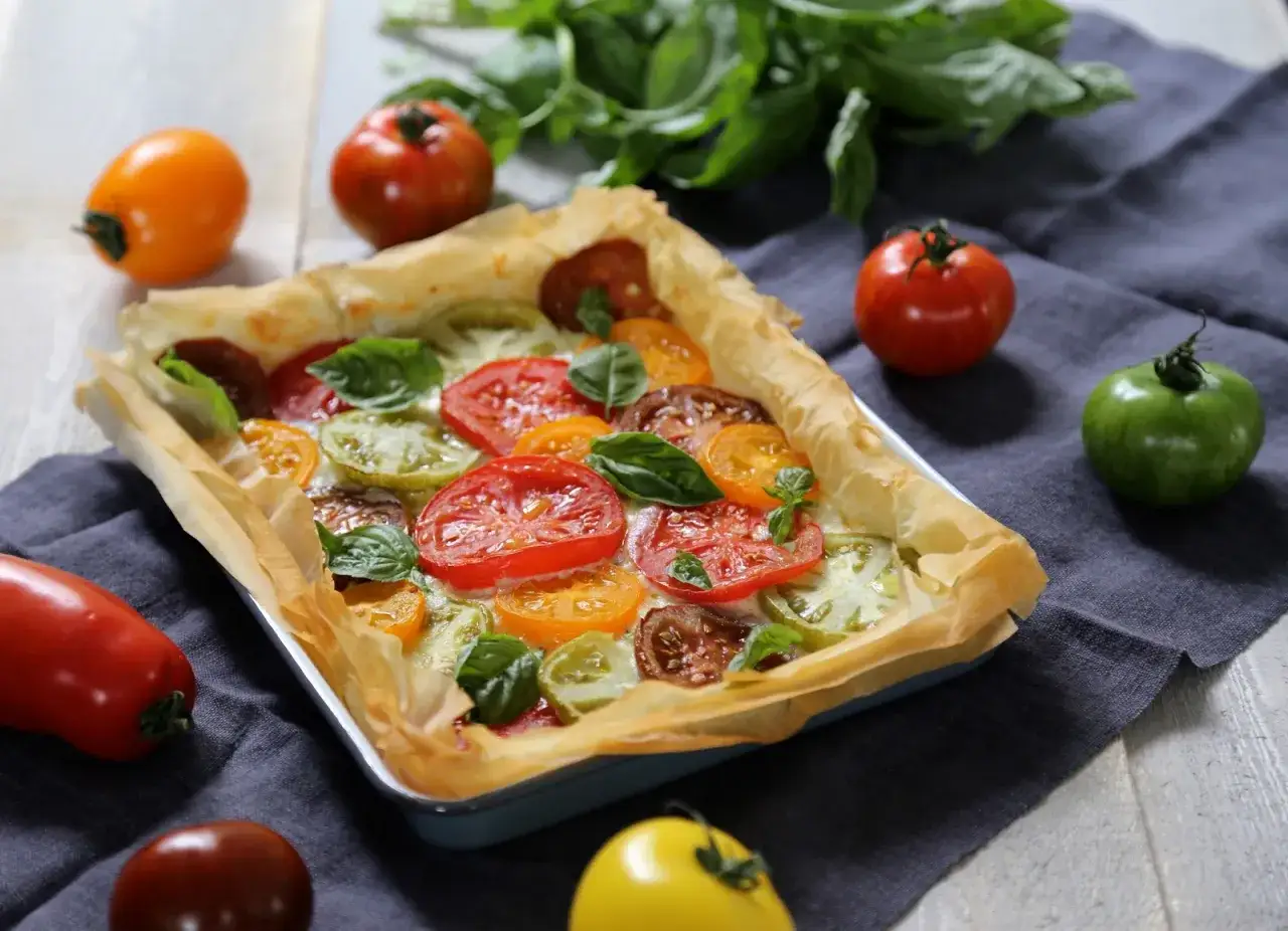 Tarte tomate chèvre aux couleurs vives, garnie de tomates variées et de feuilles de basilic frais. Un délice visuel et gustatif.