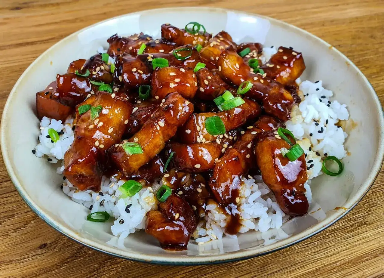 Porc au caramel, enrob&eacute; d'une sauce brillante, servi sur un lit de riz blanc parsem&eacute; de graines de s&eacute;same et d'oignons verts. Un d&eacute;lice !