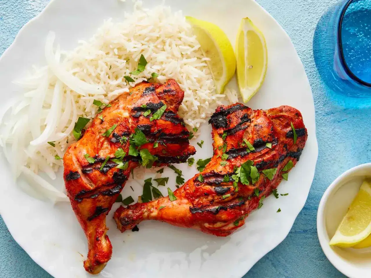 Deux morceaux de poulet tandoori grillé, servis avec du riz basmati, des oignons émincés et des quartiers de citron.