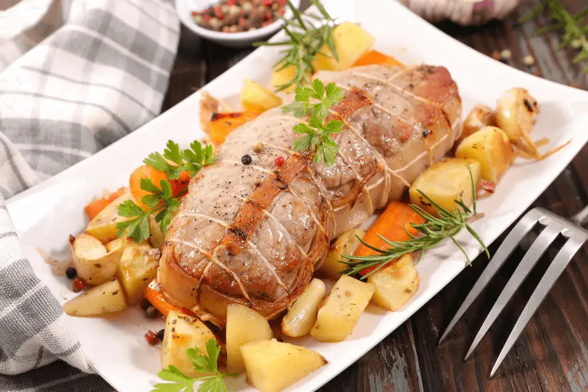 Un délicieux roti de veau, ficelé et rôti à la perfection, servi avec des pommes de terre et des carottes rôties, garni de persil frais.