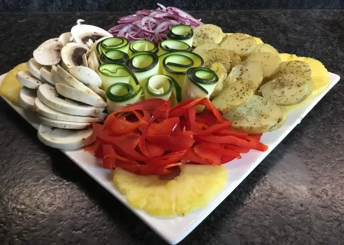 Assortiment de légumes frais et fruits pour une plancha de Noël : champignons, courgettes enroulées, poivrons rouges, pommes de terre et ananas.