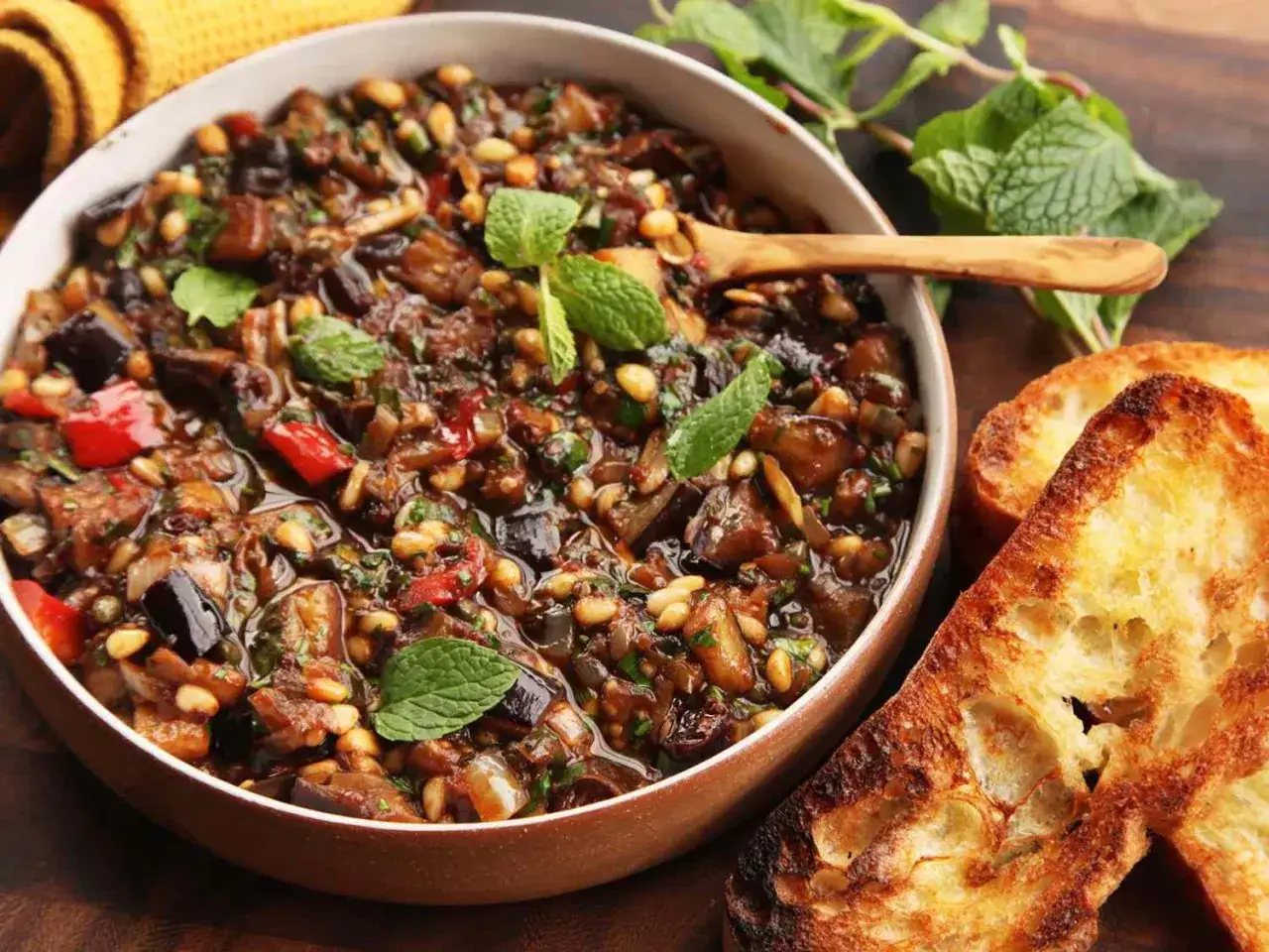 Un plat de caponata recette, avec des aubergines, poivrons, pignons de pin et menthe fraîche, servi avec du pain grillé.