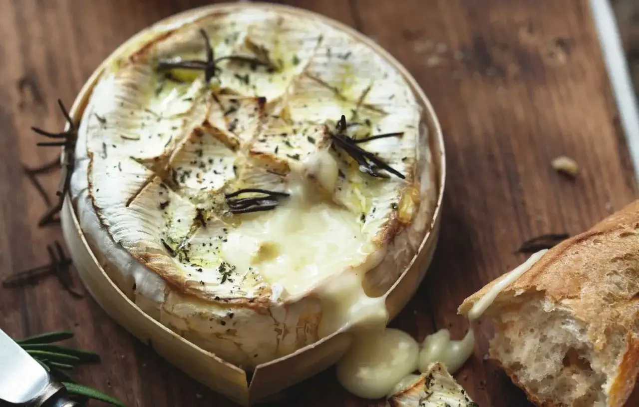 Camembert au barbecue fondant, garni de romarin, prêt à être dégusté avec une baguette croustillante.