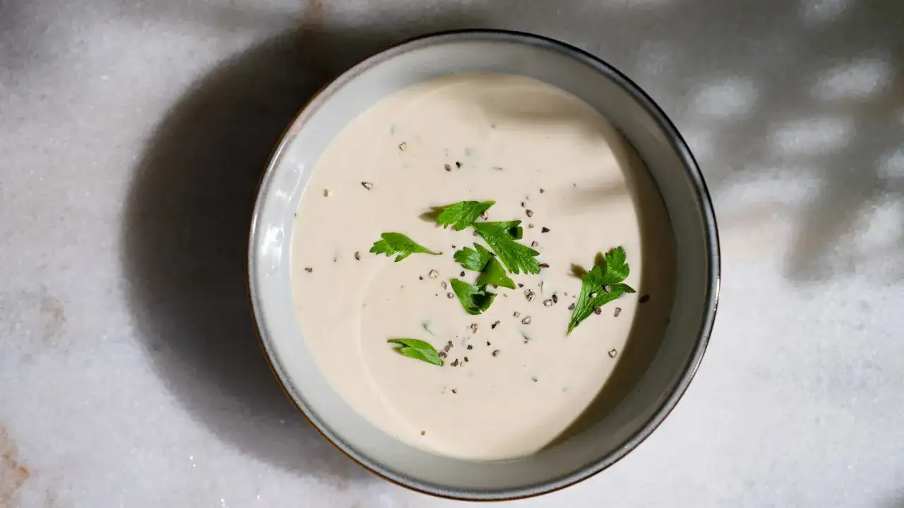 Sauce tahini crémeuse, garnie de persil frais et de poivre noir concassé, dans un bol sur fond de marbre.