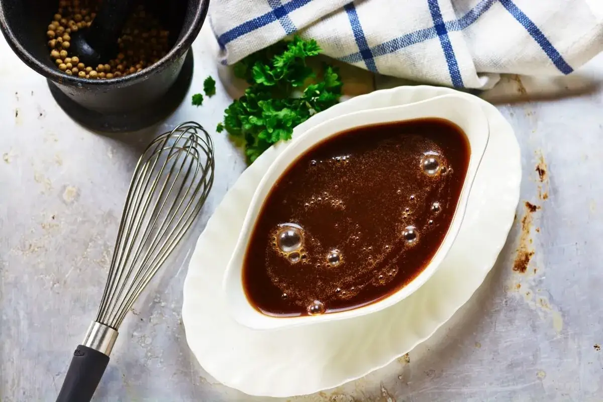 Sauce epaisse viande, riche et savoureuse, prête à être servie. Un fouet et des grains de poivre rappellent sa préparation.