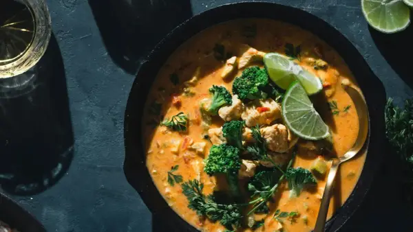 Un plat de poulet et brocolis baignant dans une sauce curry crémeuse, garni de quartiers de citron vert et de persil frais. Un délice !
