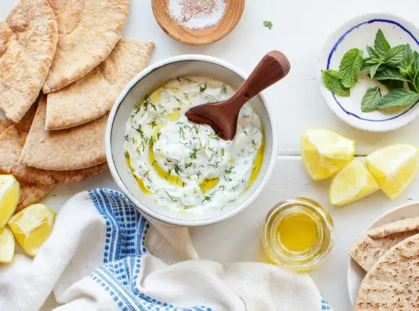 Un bol de tzatziki crémeux, garni d'aneth et d'huile d'olive, prêt à être dégusté avec du pain pita. Une recette fraîche et savoureuse.