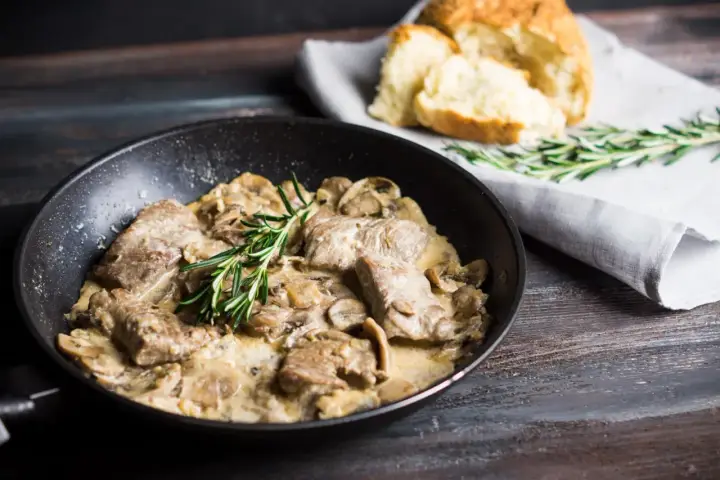 Délicieux sauté de porc crémeux aux champignons, garni de romarin frais, servi dans une poêle avec du pain croustillant à côté.