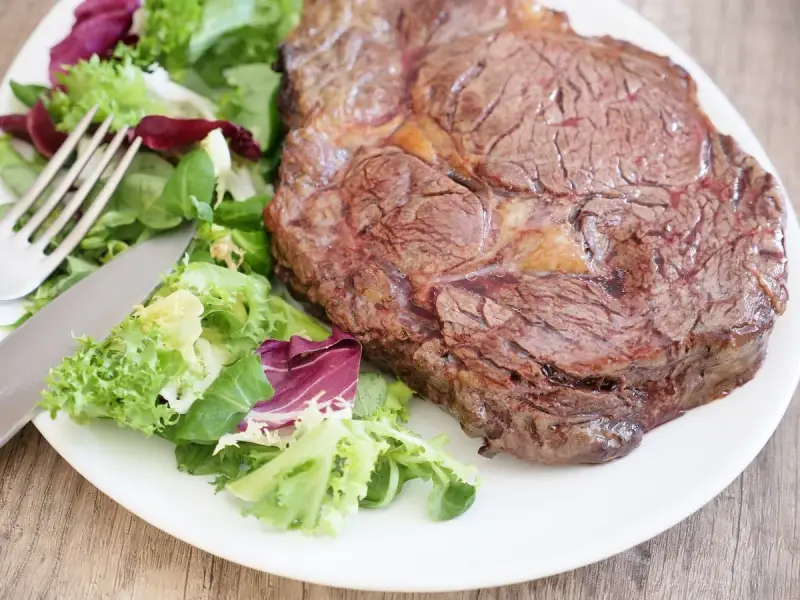 Une belle côte de bœuf juteuse, prête à être dégustée, accompagnée d'une salade fraîche. Parfait pour préparer un repas savoureux.