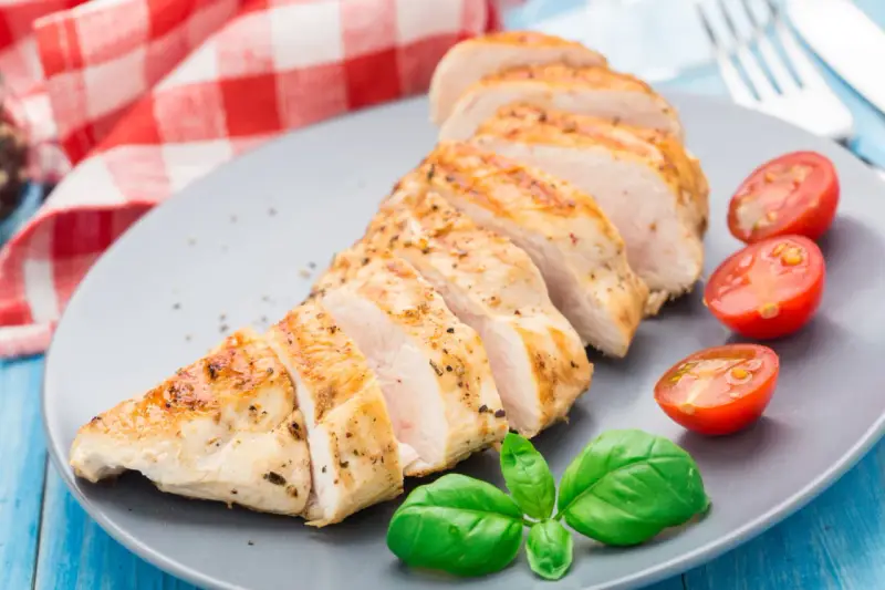 Un délicieux filet de poulet grillé, tranché et servi avec des tomates cerises et du basilic frais sur une assiette grise.